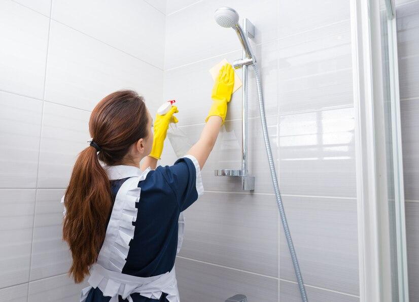 housekeeper-cleaning-shower-head-bathroom-reaching-up-wipe-it-as-she-sprays-it-with-detergent-rear-view_385506-6053.jpg